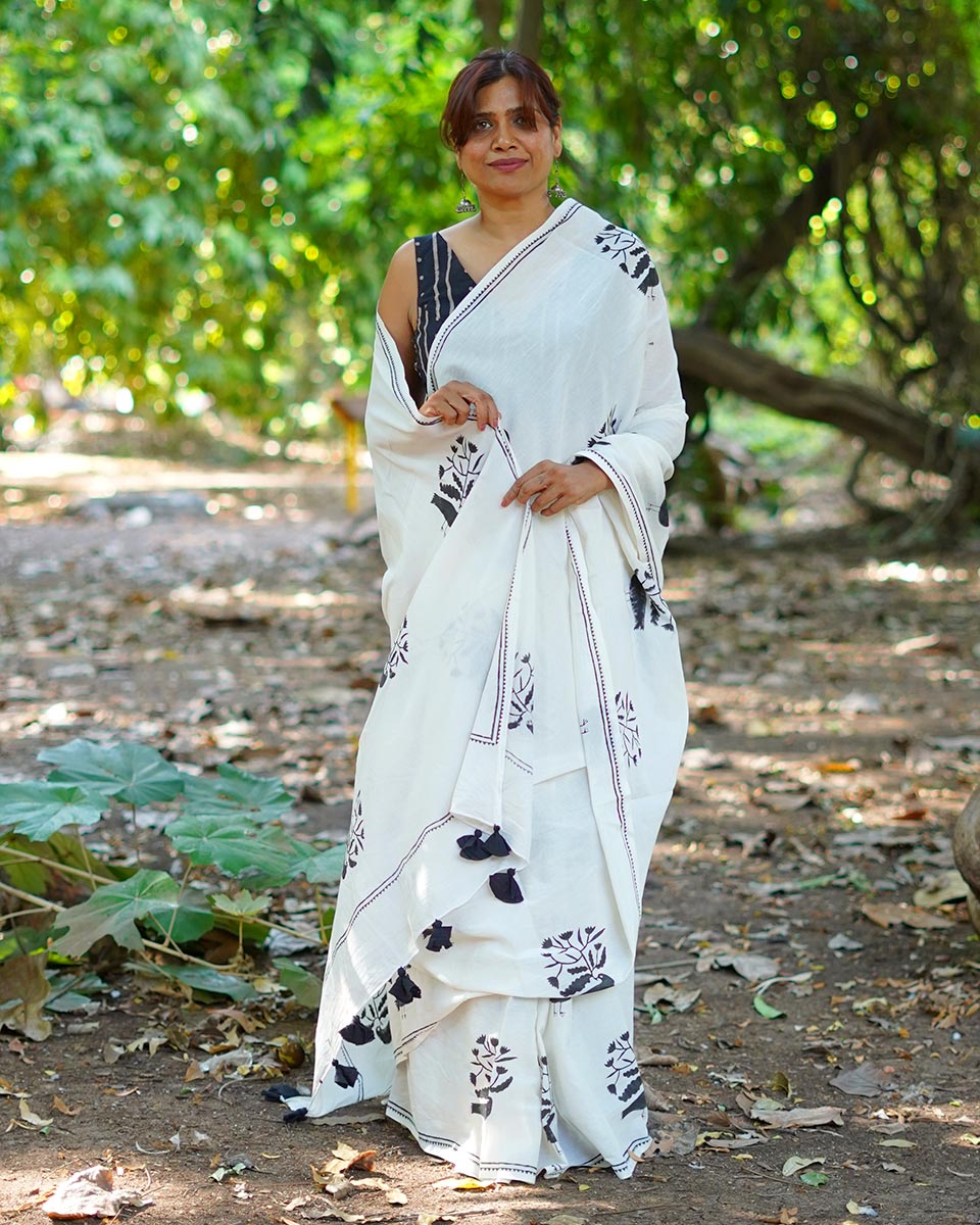 Woman wearing a white saree with black patterns standing in a natural setting.| cotton saree online shopping |soft cotton saree